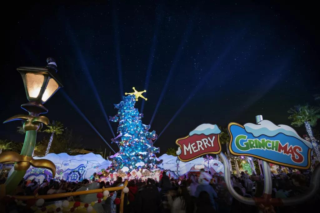 A sign reading Merry Grinchmas in front of a tall Christmas tree that curves at the top