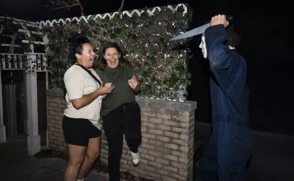 Two women screaming while a scare actor jumps out at them with a knife