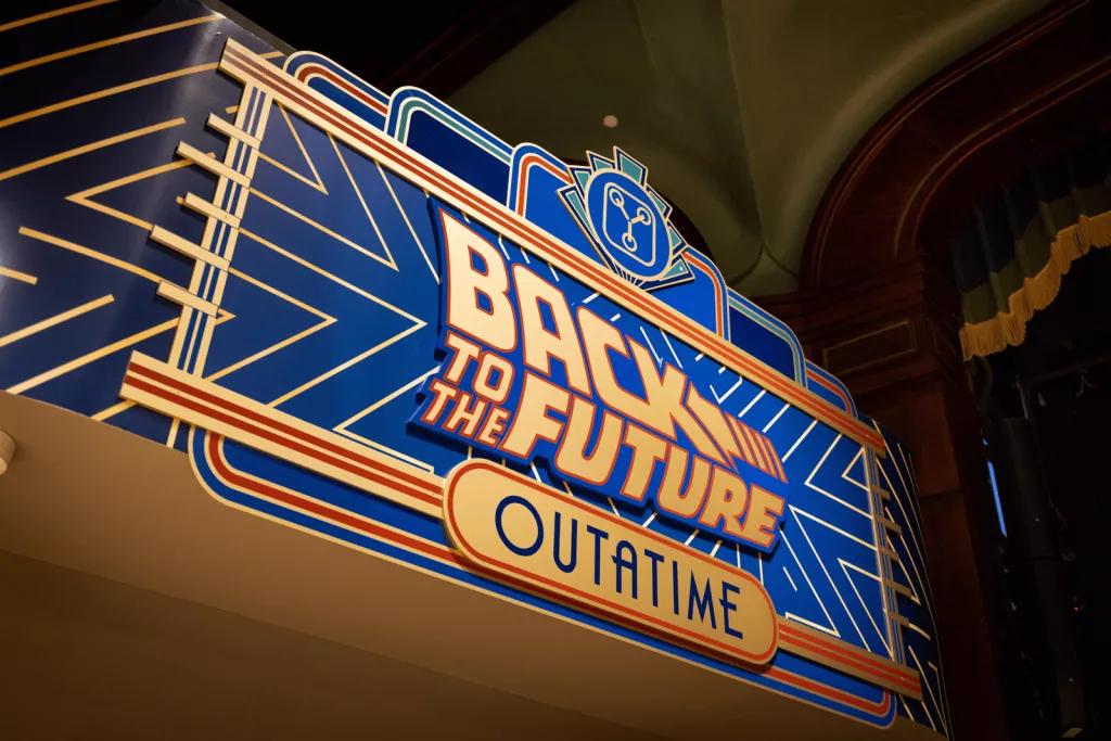 An art deco style blue and gold sign that reads "Back to the Future - OUTATIME"