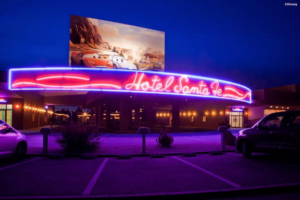 The exterior of the Hotel Santa Fe with neon letters and a billboard featuring characters from Cars