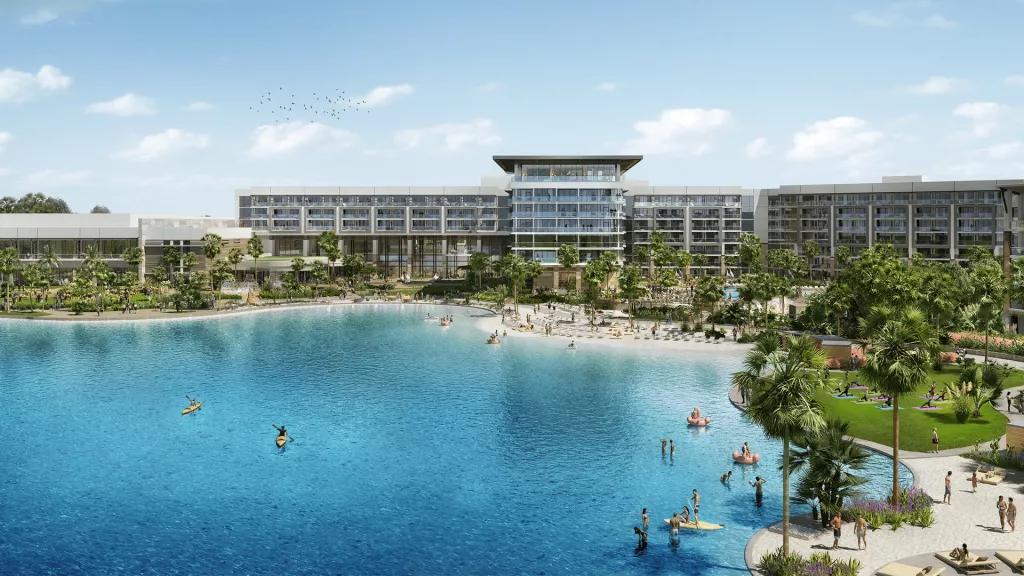 A large modern hotel building behind a lagoon with a beach and palm trees 