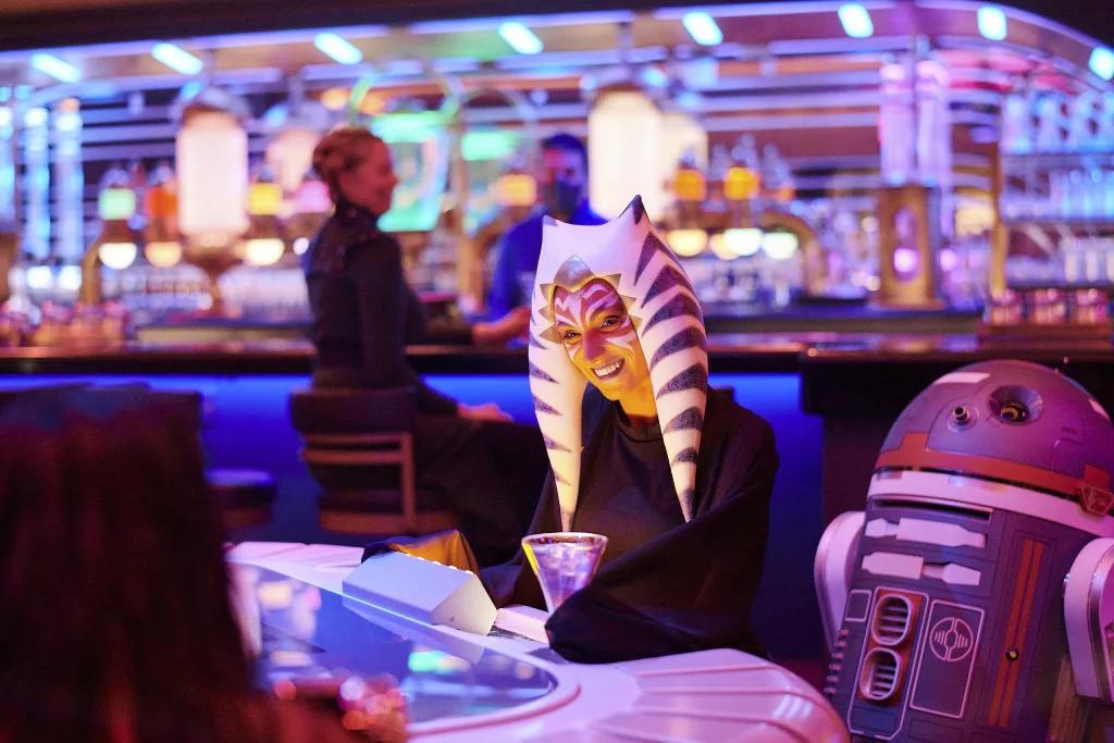 A Togruta Star Wars character drinking a cocktail next to a droid on the Galactic StarCruiser