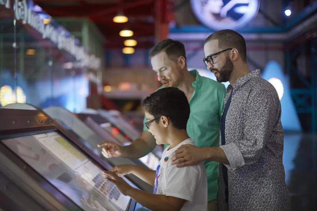 A young boy and two men using an interactive touch screen
