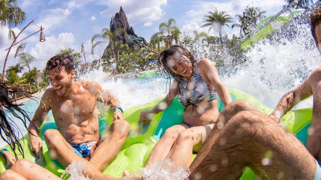 A group of guests riding a waterslide in a green raft with a volcano in the background