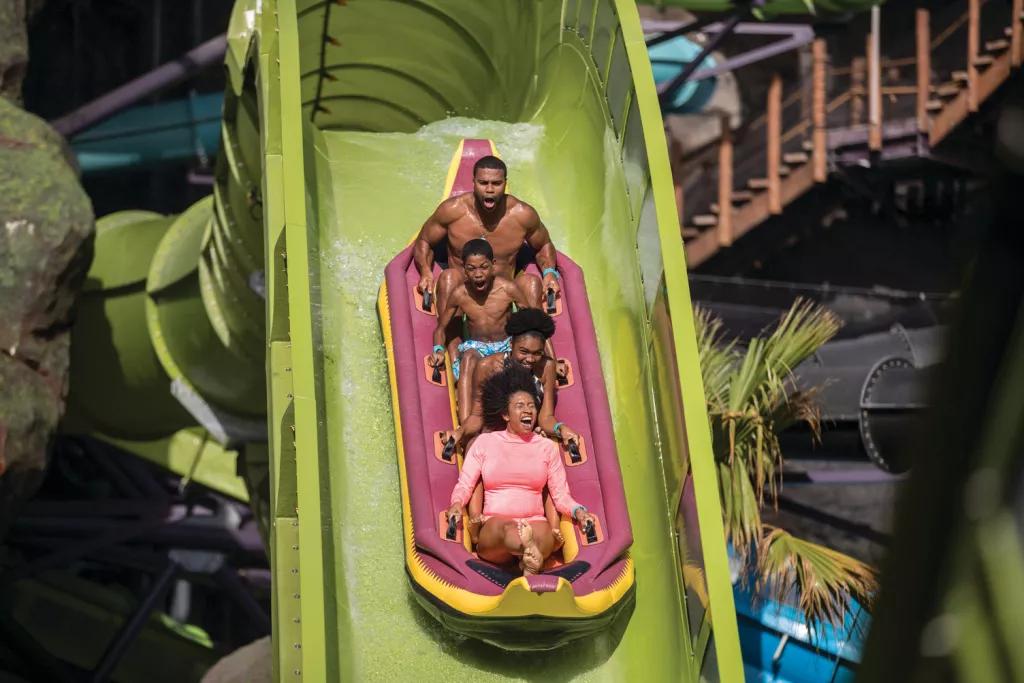 Four guests in a raft screaming as they go down a drop on the Krakatau Aqua Coaster