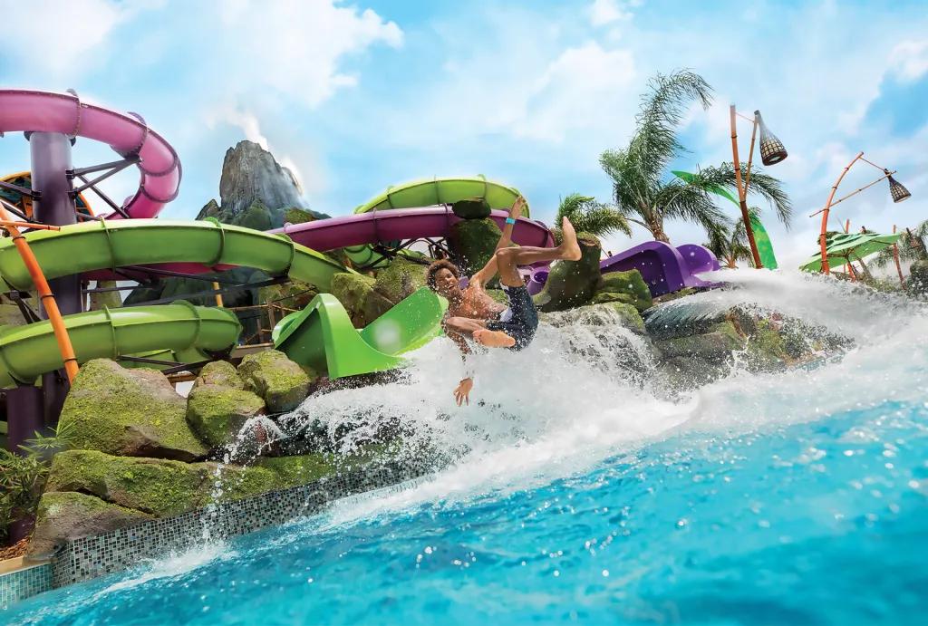 A man coming out of a waterslide about to land in a pool