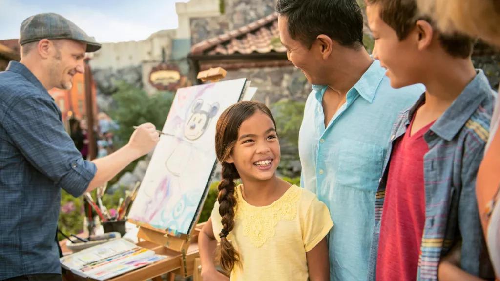 A family watching a man paint a picture of Mickey Mouse on an easel 