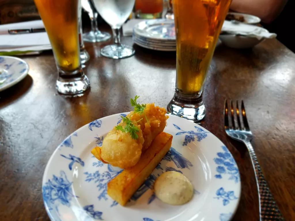A plate of fish and chips on a table next to two pints of beer