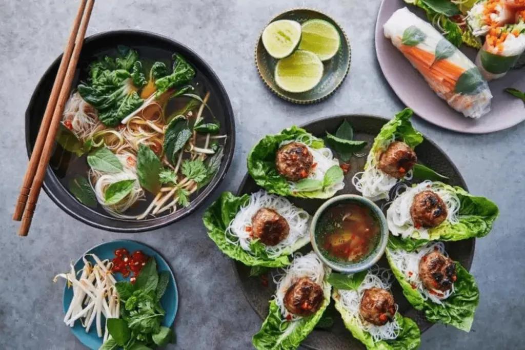 Multiple plates of Vietnamese food like spring rolls, noodle soup and lettuce wraps