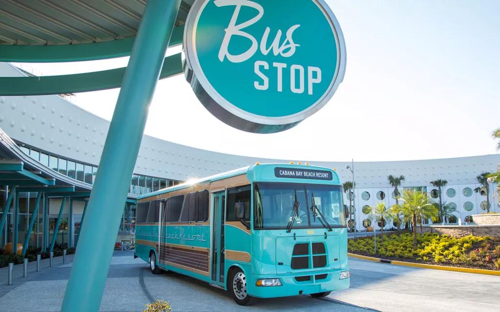 A bright blue bus waiting next to a Bus Stop sign