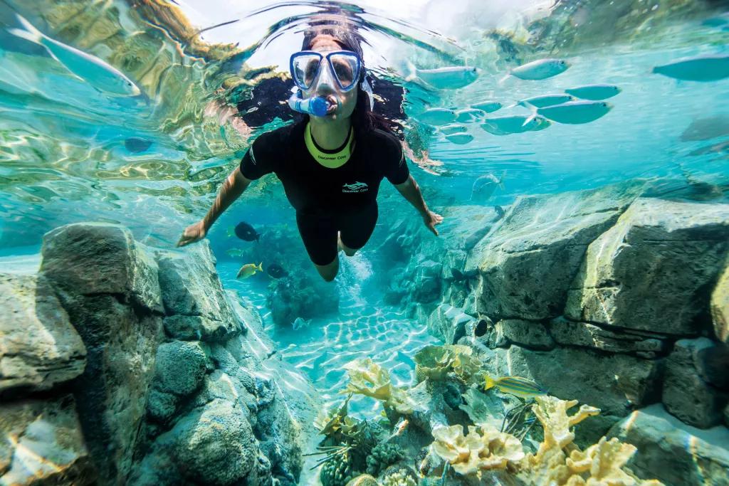A woman in a wetsuit snorkelling in clear blue water above coral reefs