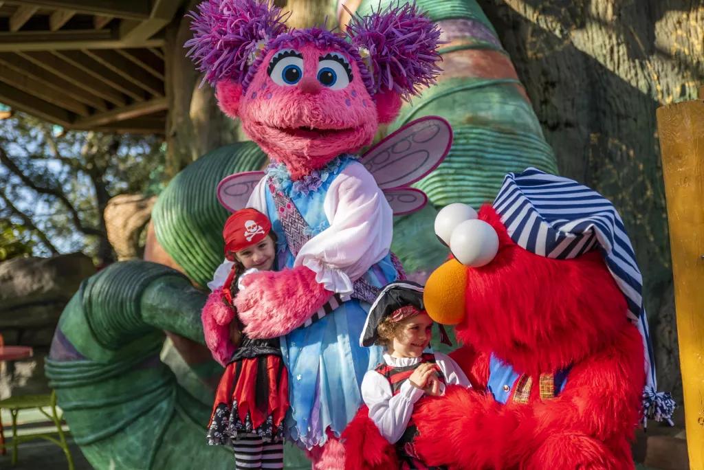 Elmo and Abby Cadabby dressed as pirates hugging two young children