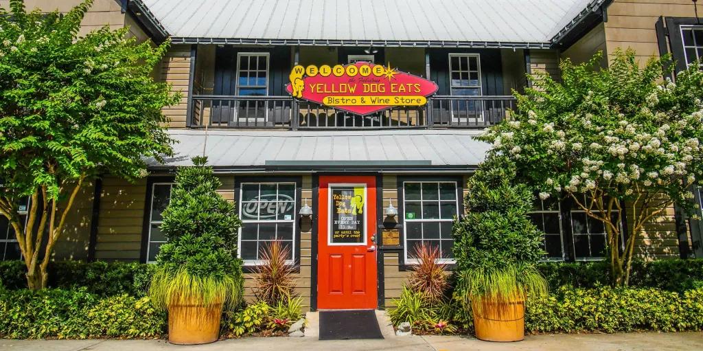 The exterior of a restaurant with a red front door and a sign reading Welcome to Yellow Dog Eats above it