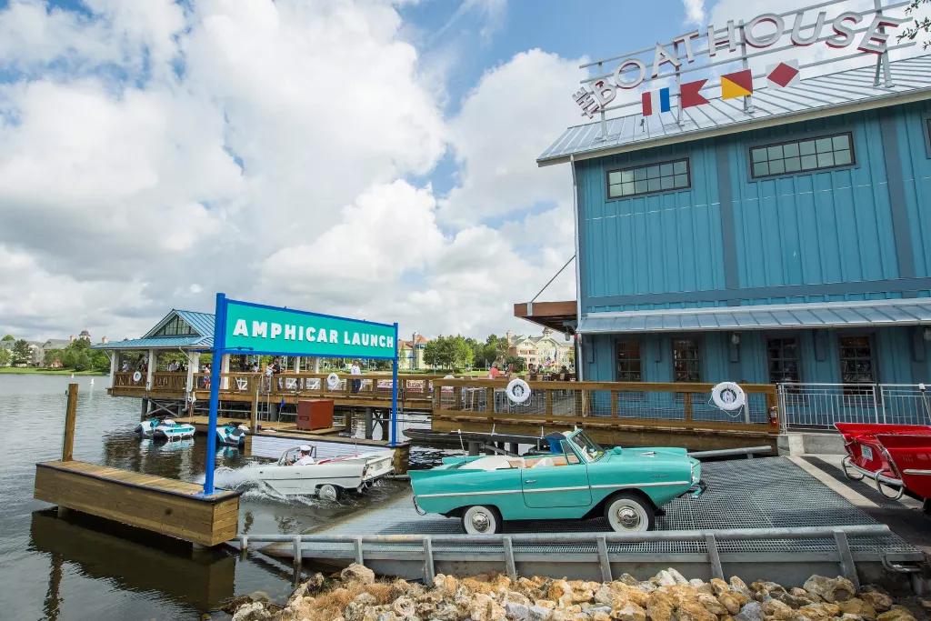 Amphicars on a ramp leading into a lake in front of a blue panelled building with a sign reading Boathouse