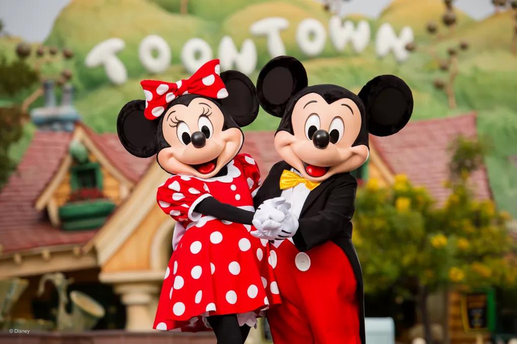 Mickey and Minnie Mouse holding hands, standing in front of a cartoon 'Toon Town' sign