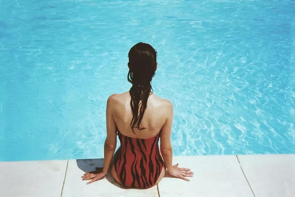 A woman wearing a swimming costume sat on the edge of a pool with her feet in the water