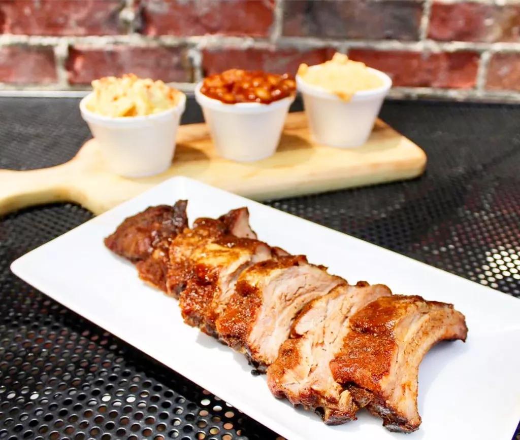 A plate of barbecued meat in front of a range of sides including baked beans and mac & cheese