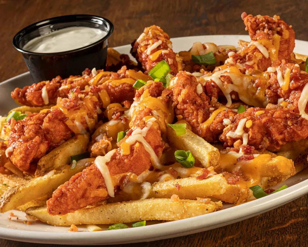 A large plate of fries topped with breaded chicken tenders and cheese