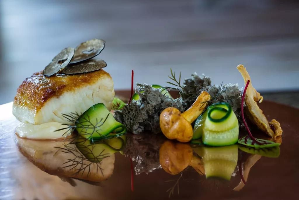 A plate of fish and curled strips of vegetables finished with a herb garnish
