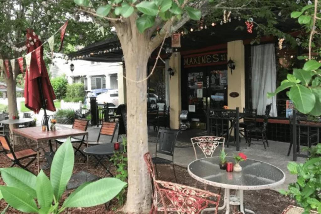 The exterior of a restaurant with tables and mismatched chairs and a tree lit with fairy lights on the pavement