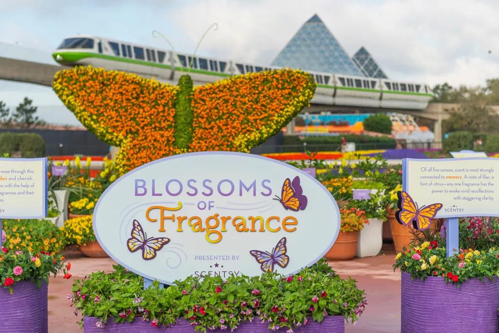 A sign reading Blossoms of Fragrance in front of a large butterfly made of flowers and a monorail overhead