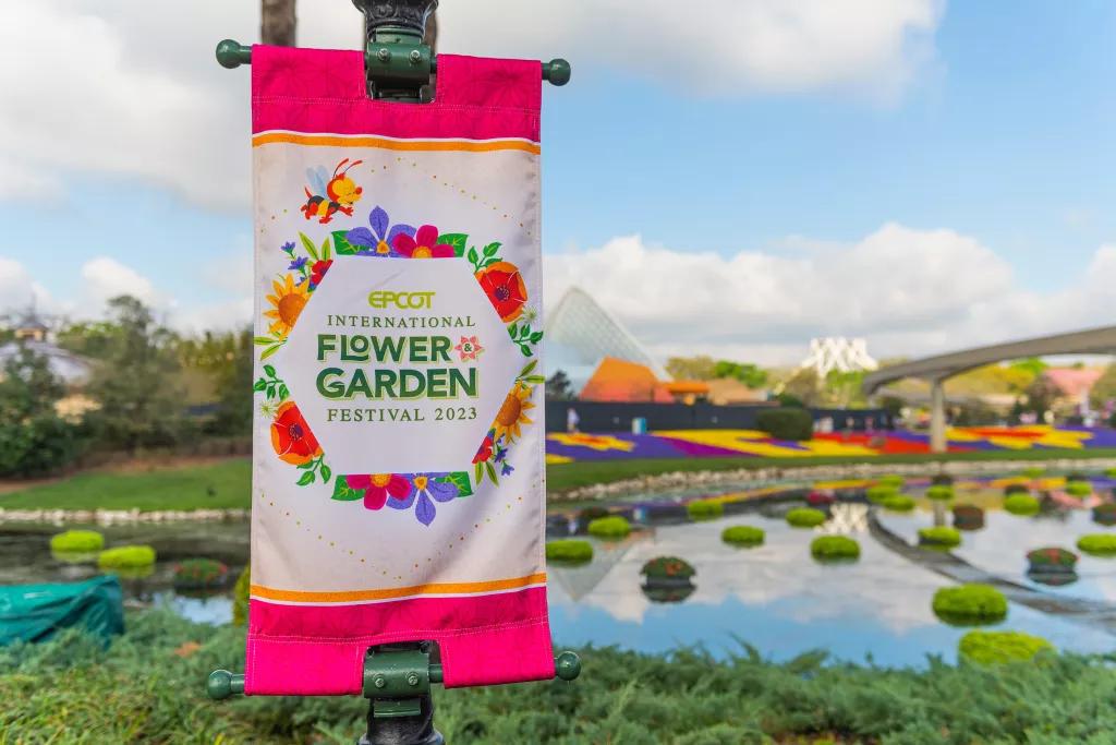 A sign reading EPCOT Flower and Garden Festival in front of a blue sky and flower beds