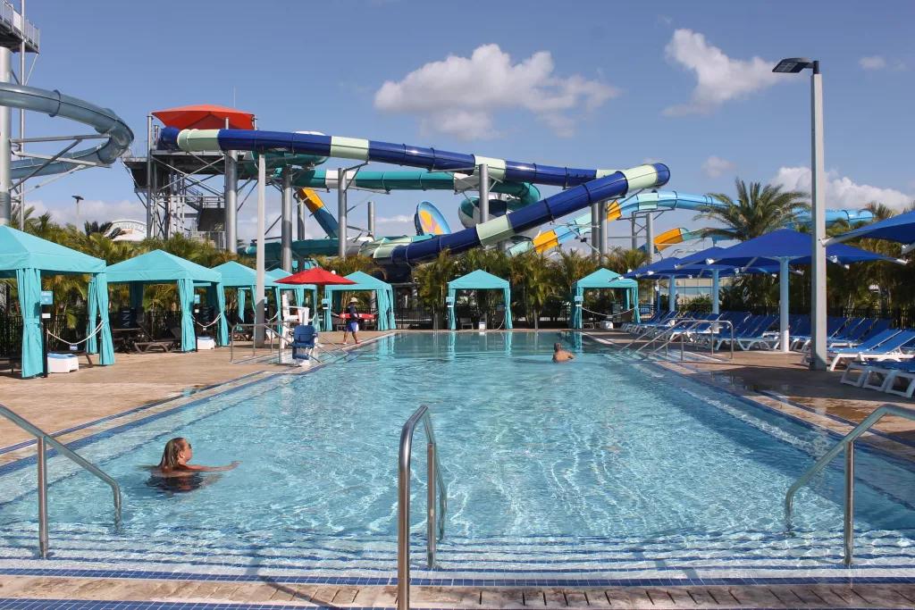 A rectangular pool adults-only pool with large water slides in the background
