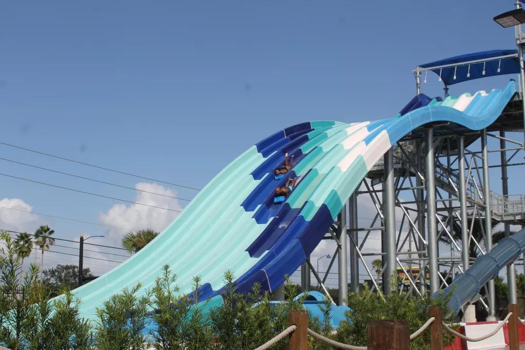 A blue striped water slide with two people sliding down head-first on mats