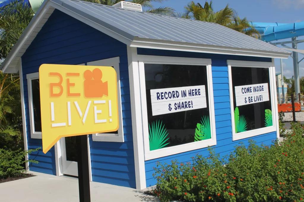 A shack with two large windows behind a sign that reads 'Be Live' 
