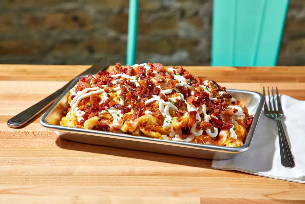 A metal tray piled high with waffle fries topped with bacon, cheese and sour cream