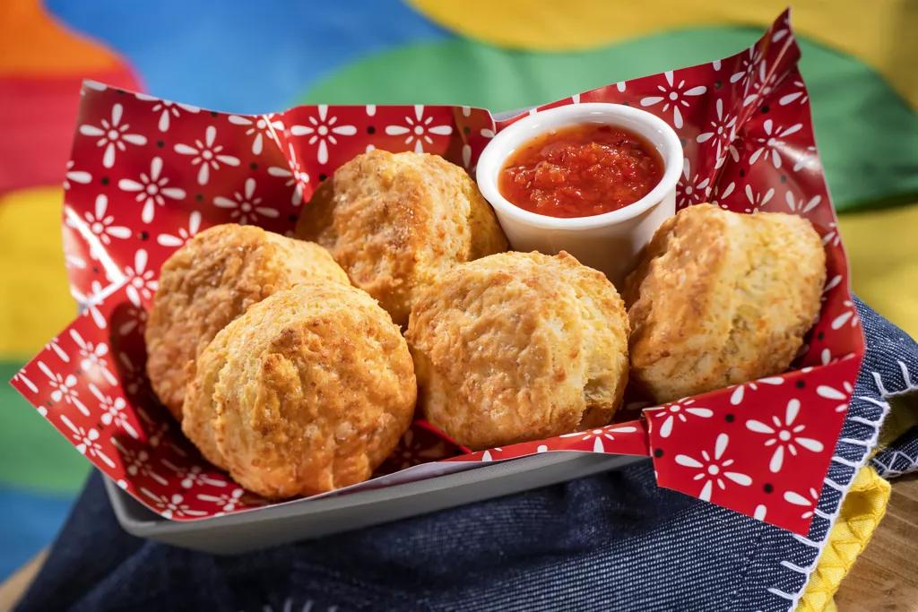 A basket full of cheddar biscuits with a ramekin of pepper jelly