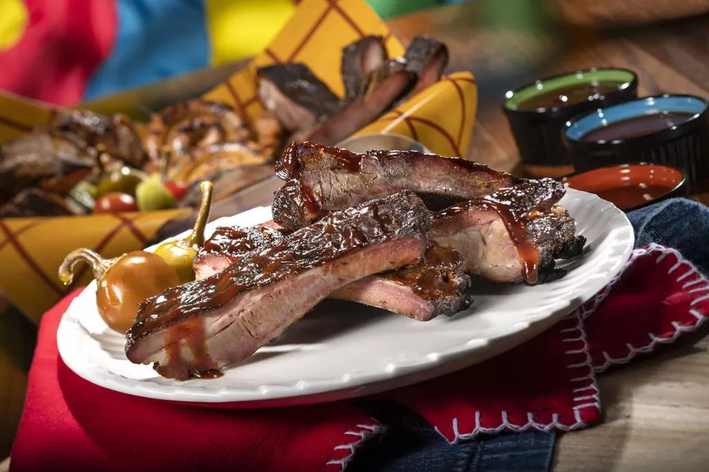 A plate full of barbecued ribs in front of a basket of other meats