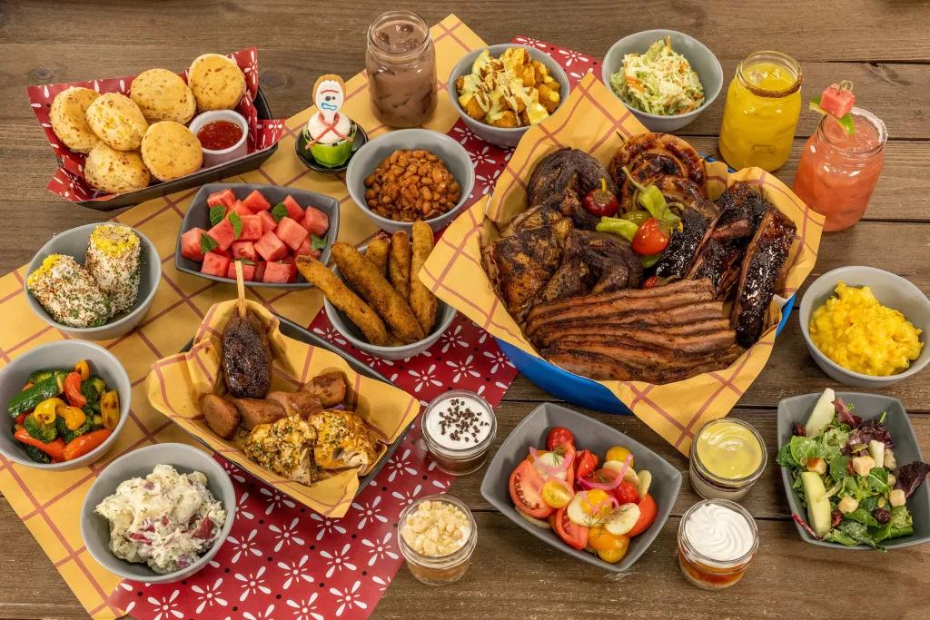 A birds eye view of a plate full of barbecue food including a plate of meats, salads, corn on the cob and desserts