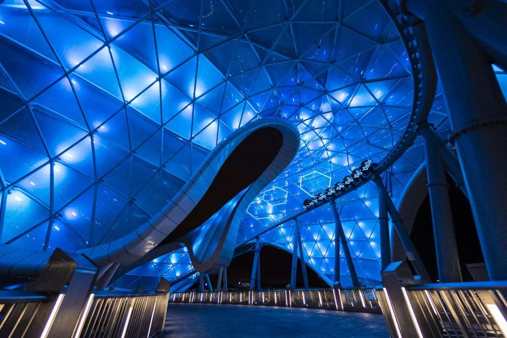 A wide shot of TRON Lightcycle / Run underneath a lit up canopy at night 