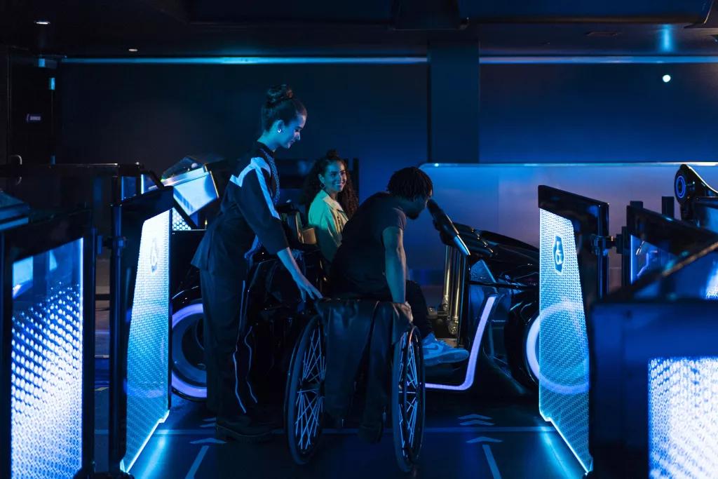 A Cast Member helping a man out of a wheelchair into a TRON ride vehicle