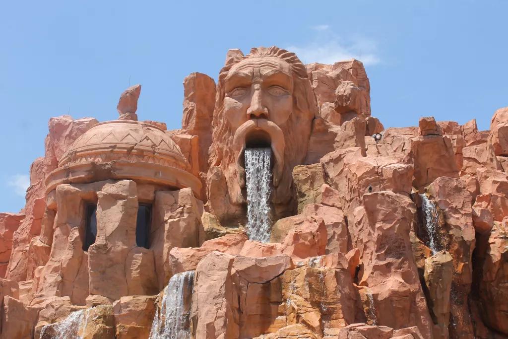 A rock formation carved to look like a face with a waterfall coming out of the open mouth