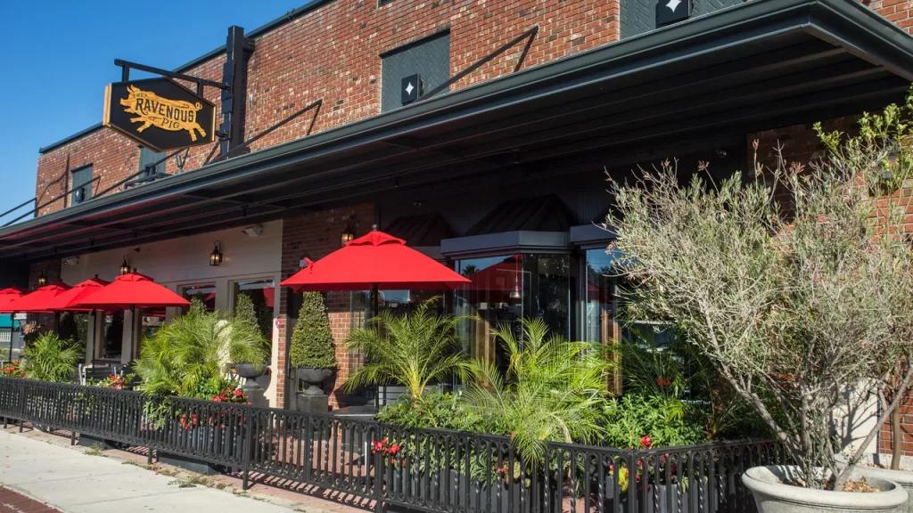 The exterior of a brick building with a patio covered by red umbrellas