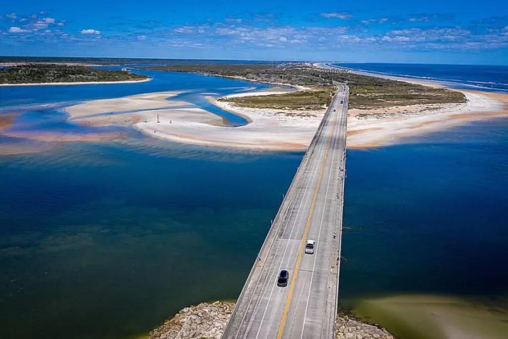 Bird's eye view of a highway going over some bright blue water between two islands