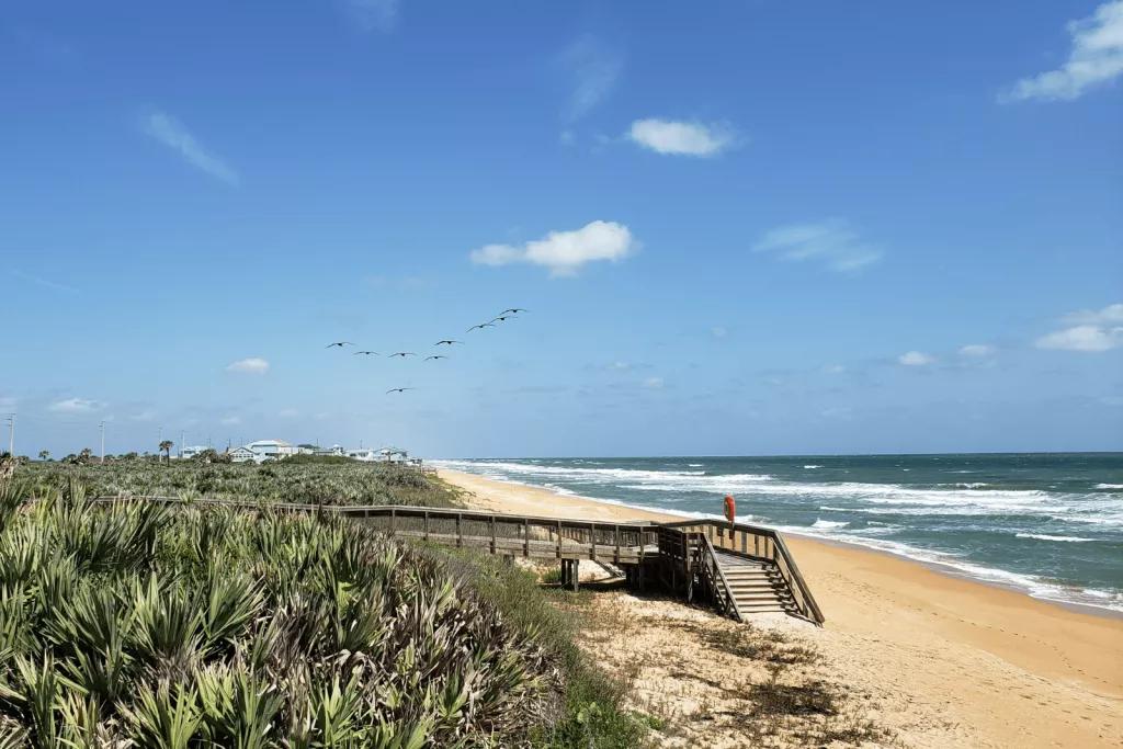 A wooden walkway leading down to a sandy beach and blue ocean