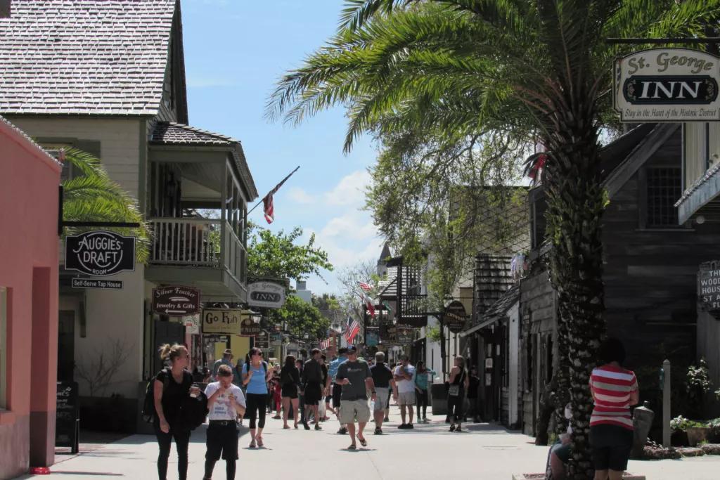 A pedestrian street full of people, lined with palm trees and shops