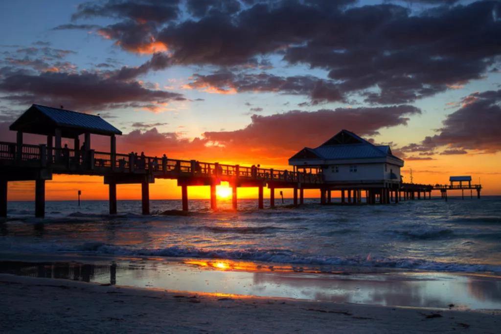 A sunset behind a pier leading out from Clearwater Beach into the ocean