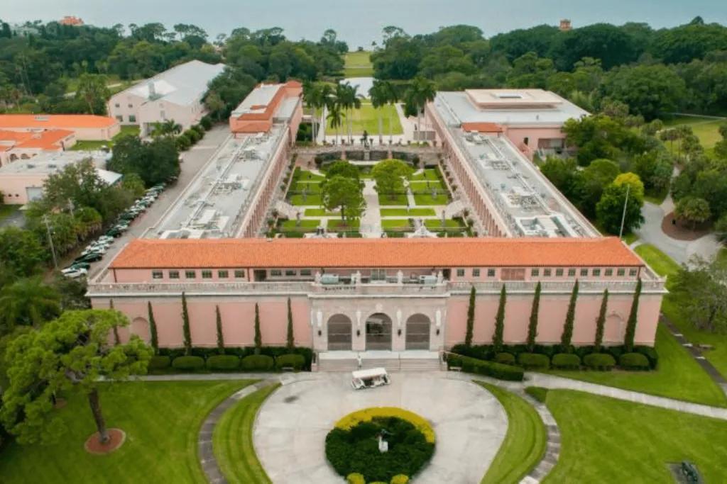 An aerial view of a roman-style building surrounding a courtyard with the sea in the background