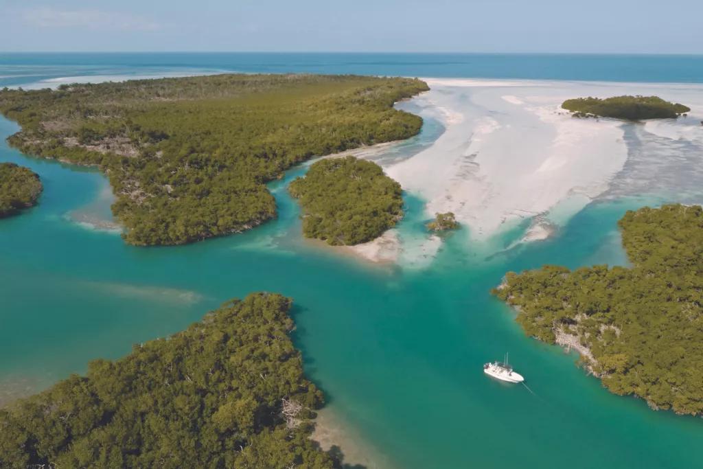 An aerial view of a boat sailing through the teal waters between the sandy islands of the Florida Keys