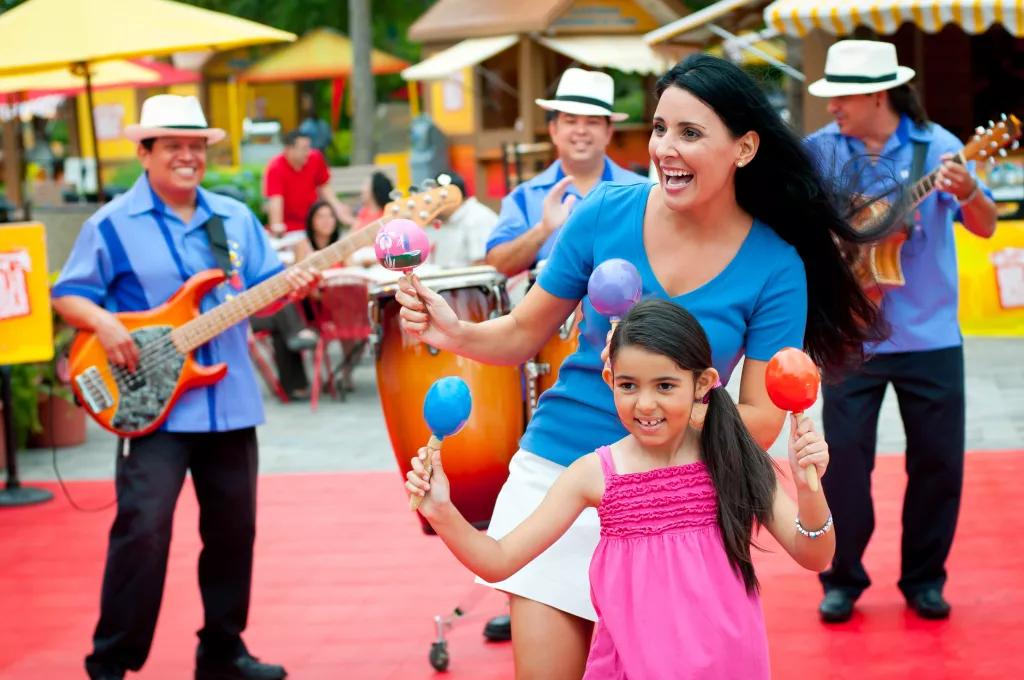 A young girl and a woman dancing in front of a band while shaking maracas 