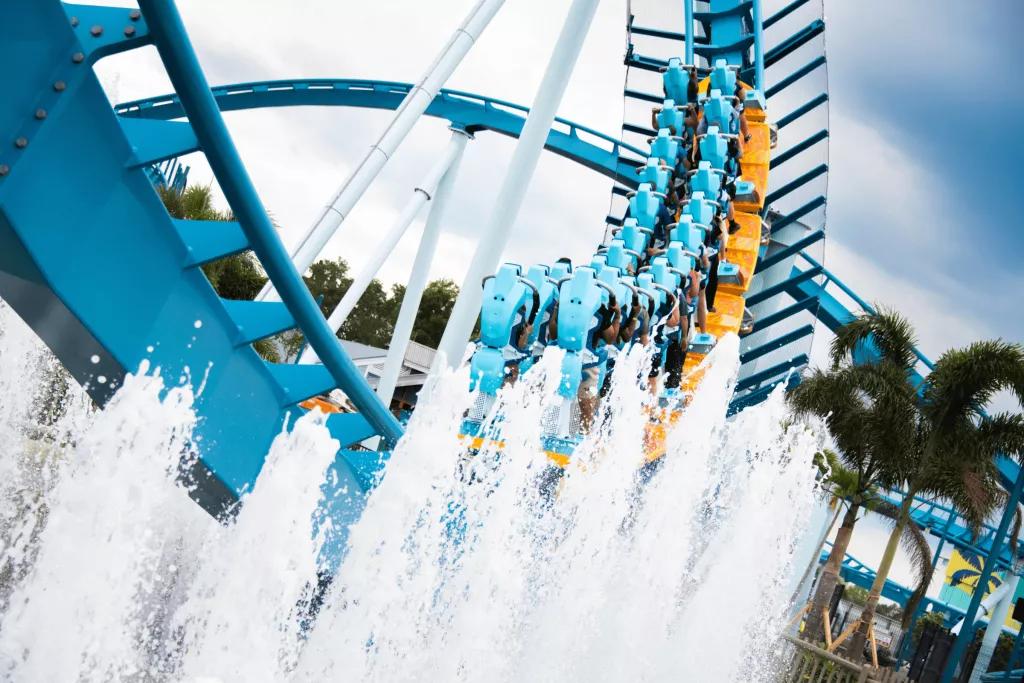 A yellow ride vehicle on a blue rollercoaster track heading away from the camera as water rises up from fountains