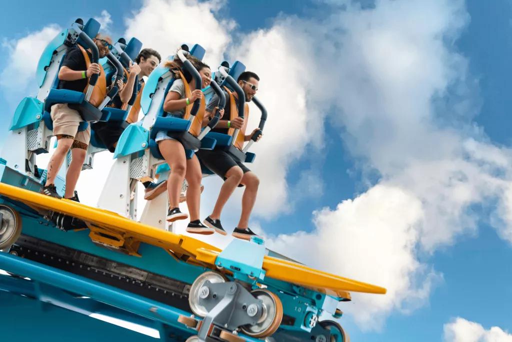Four people standing on a rollercoaster ride vehicle being held up by restraints