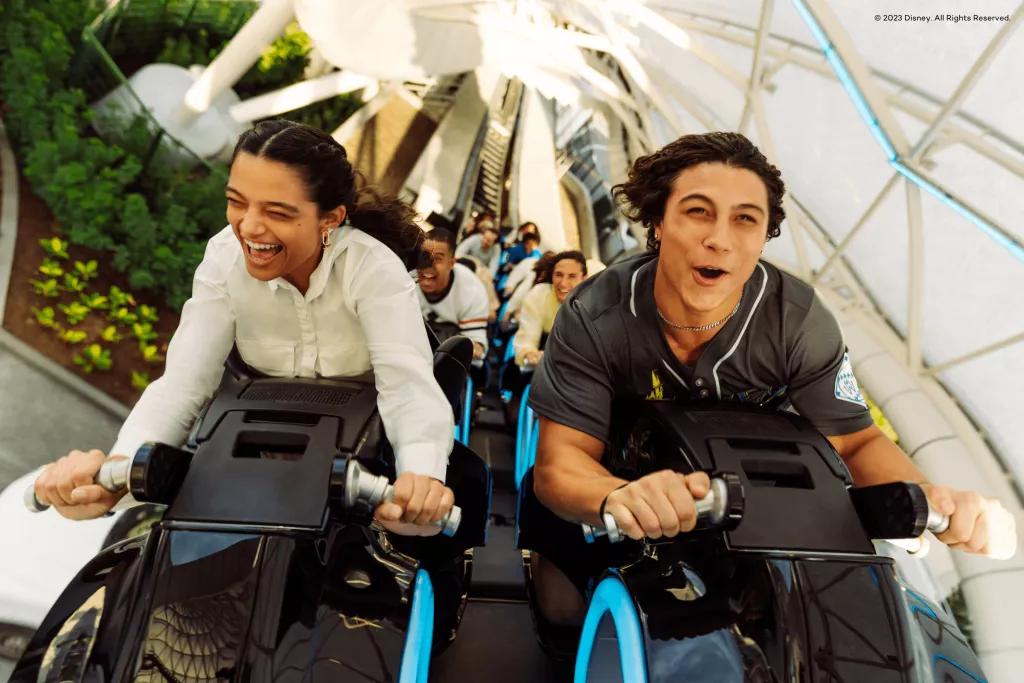 A man and woman smiling while riding TRON at Disney World on ride vehicles shaped like motorbikes