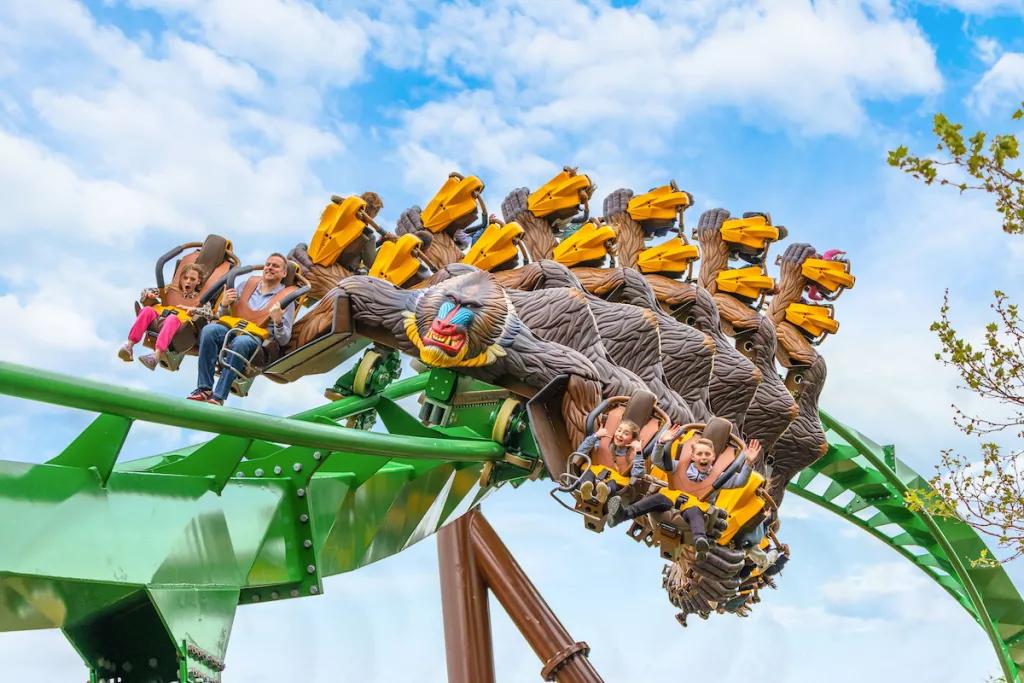 People riding a rollercoaster shaped like a Mandrill going along a green track