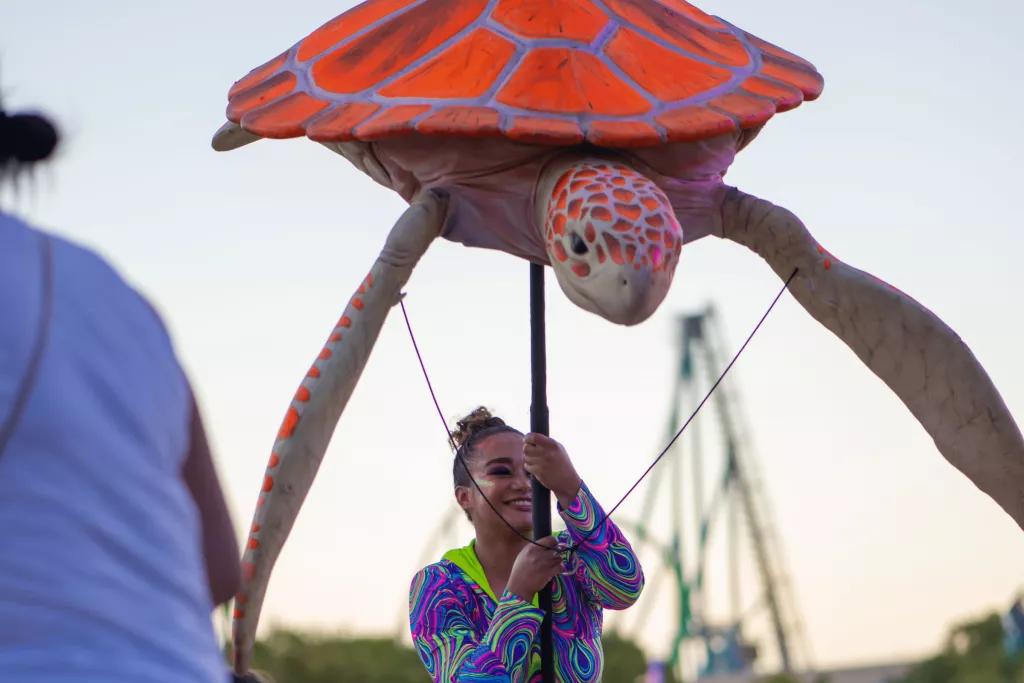 A female performer in a neon top holding a large sea turtle puppet above her head