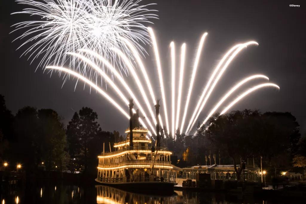 A large riverboat lit up at night with fireworks in the background